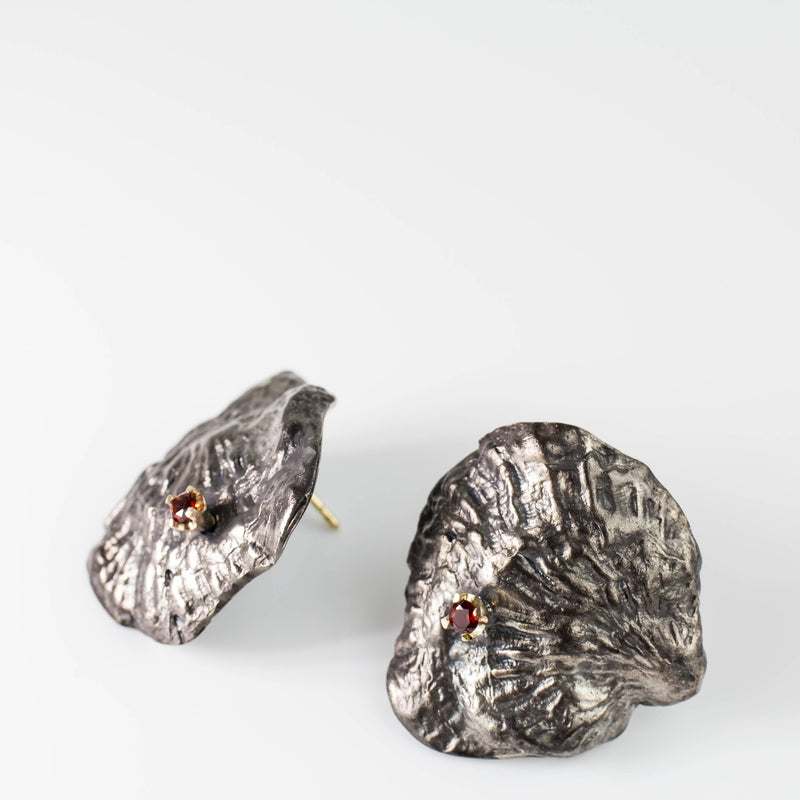 Sterling silver, 18kt gold and garnet earrings are cast from a single shell. They are large and reminiscent of an 80's power earring. Gold butterflies secure the backs. By designer Tamahra Prowse