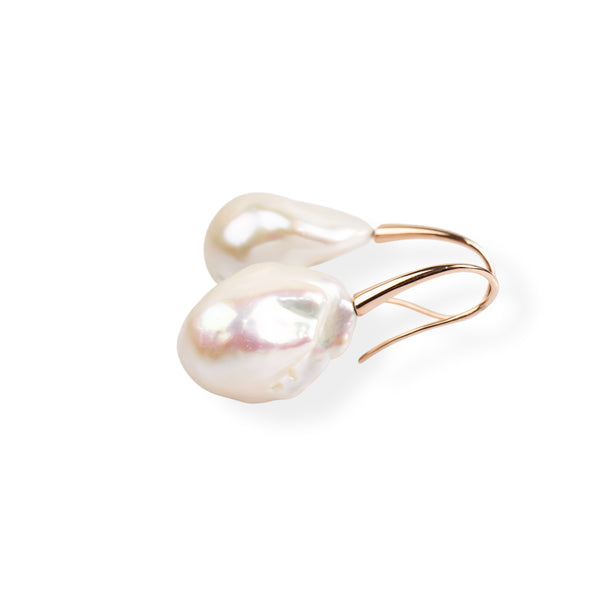 A pair of baroque pearl earrings with rose gold hooks against a white background.