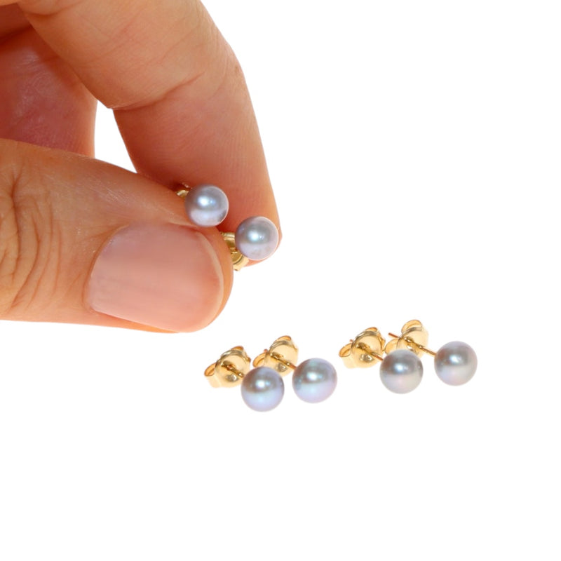 Gold and silver akoya pearl stud earrings held by a hand on a white background